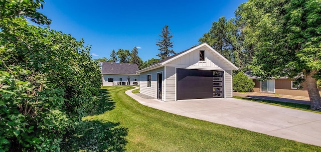 view of front facade with a front yard, an outbuilding, concrete driveway, a detached garage, and board and batten siding