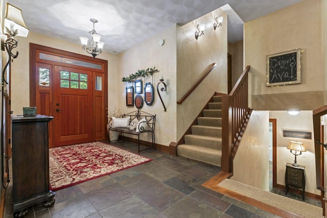 foyer entrance featuring a notable chandelier, baseboards, stone tile floors, and stairs