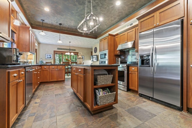 kitchen featuring stone tile floors, dark countertops, an inviting chandelier, built in appliances, and under cabinet range hood