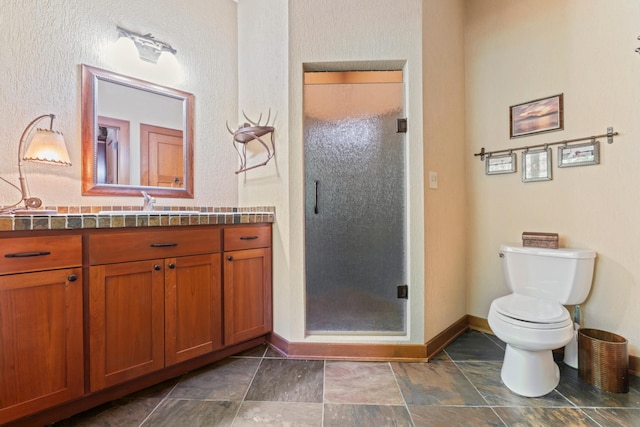 bathroom featuring a stall shower, vanity, baseboards, stone finish flooring, and toilet