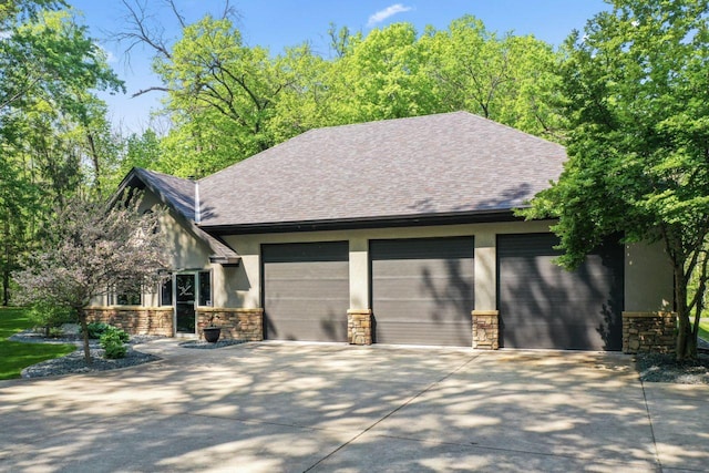 exterior space with concrete driveway, stone siding, a garage, stucco siding, and roof with shingles