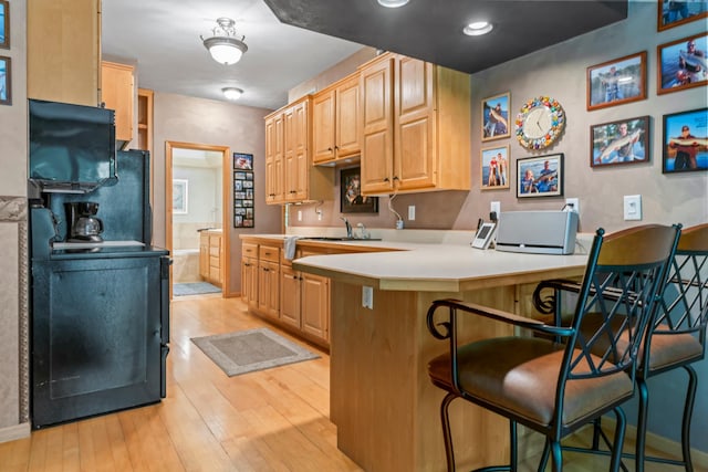kitchen with light wood finished floors, a peninsula, a kitchen breakfast bar, light brown cabinetry, and a sink
