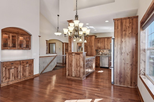 kitchen with light stone counters, pendant lighting, appliances with stainless steel finishes, brown cabinetry, and a kitchen island