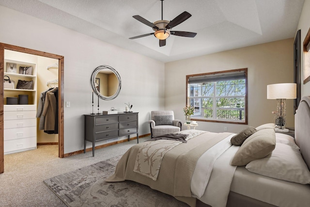 bedroom featuring light carpet, baseboards, a raised ceiling, a ceiling fan, and a spacious closet