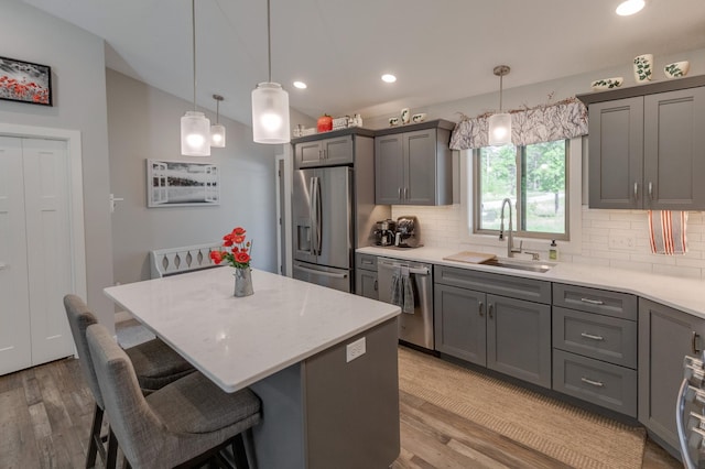 kitchen with hanging light fixtures, sink, stainless steel appliances, and light wood-type flooring