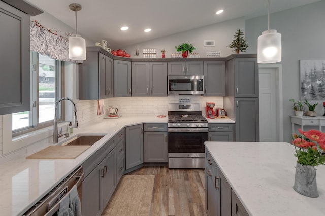 kitchen with light stone counters, hanging light fixtures, vaulted ceiling, and appliances with stainless steel finishes