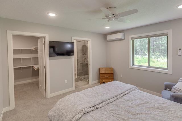 bedroom featuring a walk in closet, ensuite bathroom, a wall mounted AC, ceiling fan, and a closet