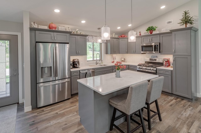 kitchen featuring appliances with stainless steel finishes, sink, a center island, hanging light fixtures, and lofted ceiling