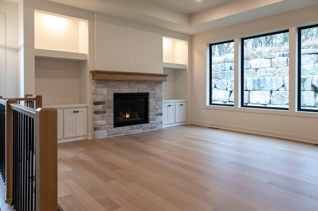 unfurnished living room with built in shelves, light hardwood / wood-style flooring, and a stone fireplace