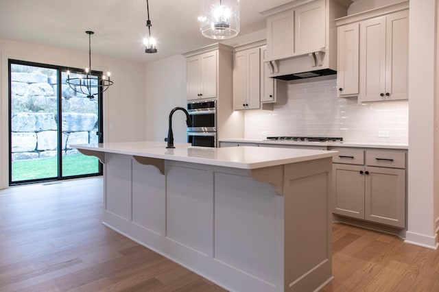 kitchen featuring a center island with sink, light hardwood / wood-style floors, appliances with stainless steel finishes, and an inviting chandelier