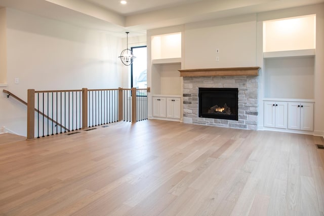 unfurnished living room featuring a stone fireplace, light hardwood / wood-style floors, and an inviting chandelier