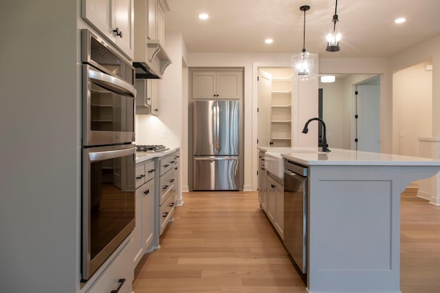 kitchen with gray cabinetry, stainless steel appliances, a kitchen island with sink, and light hardwood / wood-style flooring