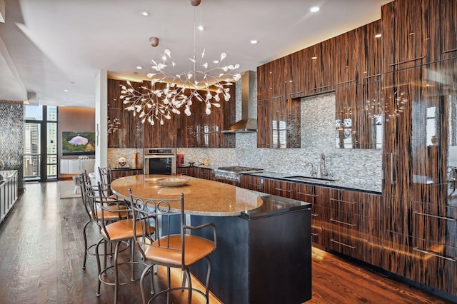 kitchen with wall chimney exhaust hood, an inviting chandelier, expansive windows, hardwood / wood-style floors, and appliances with stainless steel finishes