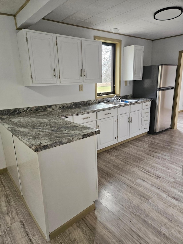 kitchen featuring dark stone counters, sink, stainless steel fridge, light hardwood / wood-style floors, and white cabinetry