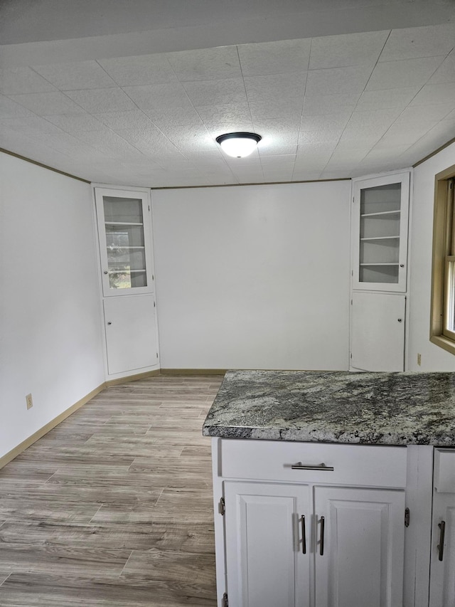 kitchen with white cabinets, dark stone countertops, built in features, and light hardwood / wood-style flooring