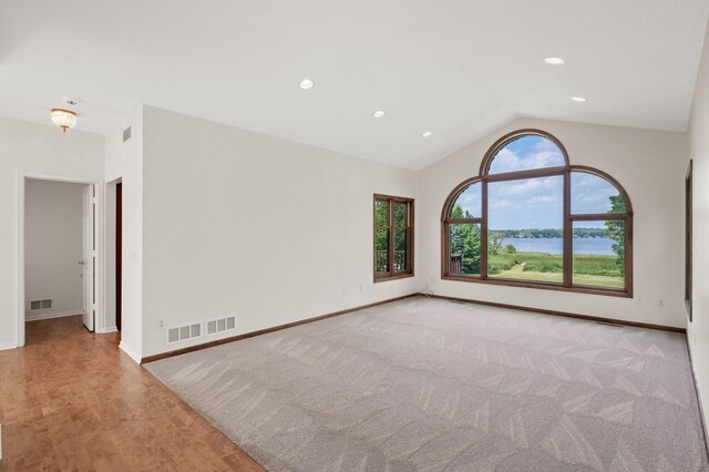 spare room featuring a water view, light hardwood / wood-style flooring, lofted ceiling, and a healthy amount of sunlight