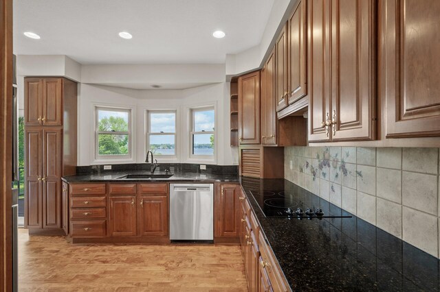 kitchen featuring light wood-type flooring, stainless steel dishwasher, sink, and dark stone countertops