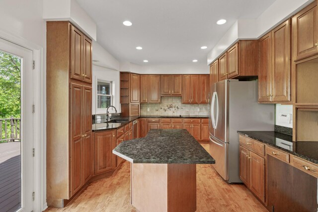 kitchen featuring backsplash, sink, light wood-type flooring, a center island, and dark stone countertops