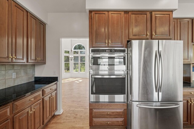 kitchen with decorative backsplash, dark stone countertops, light hardwood / wood-style flooring, and appliances with stainless steel finishes