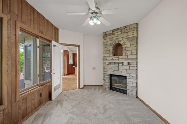 living room featuring ceiling fan, wood walls, light carpet, and a fireplace