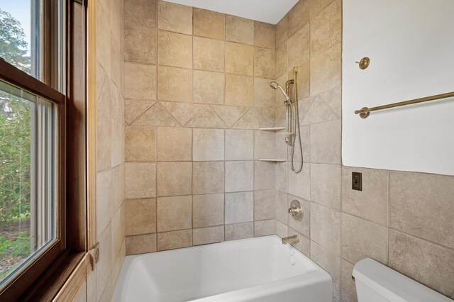 bathroom featuring tiled shower / bath, toilet, and tile walls