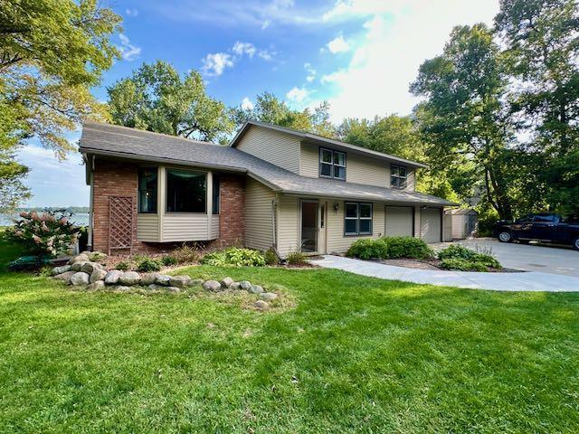 view of front facade with brick siding, driveway, and a front lawn