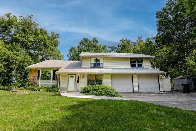 split level home with aphalt driveway, an attached garage, and a front lawn