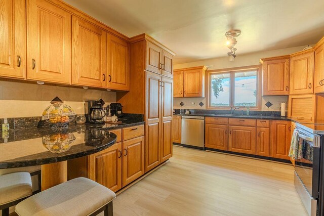 kitchen with brown cabinets, light wood-style flooring, appliances with stainless steel finishes, a sink, and dark stone counters