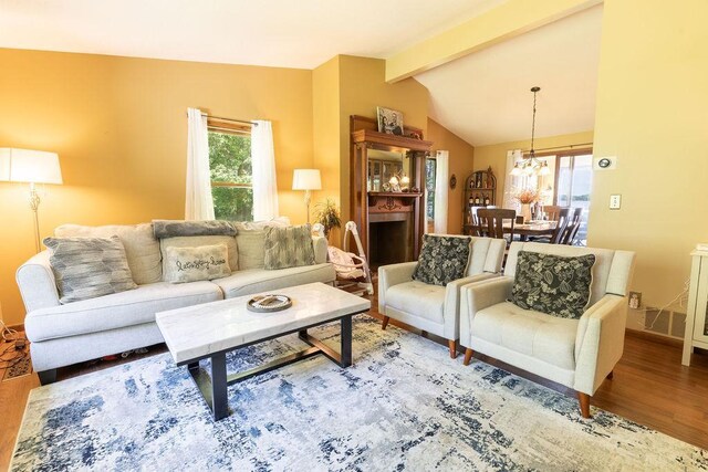 living area featuring a chandelier, vaulted ceiling with beams, baseboards, and wood finished floors