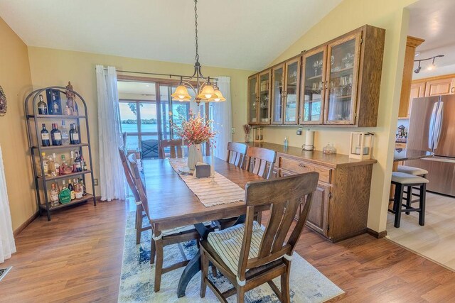 dining room with a notable chandelier, lofted ceiling, visible vents, light wood-style flooring, and baseboards