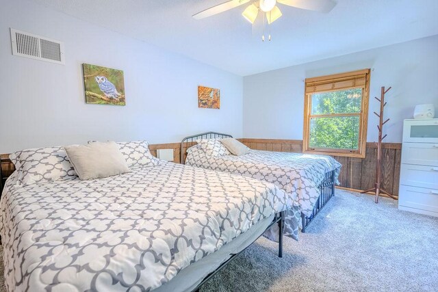 bedroom with ceiling fan, a wainscoted wall, carpet floors, wood walls, and visible vents