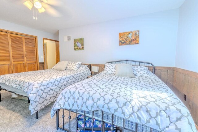 carpeted bedroom with a closet, wainscoting, and a ceiling fan