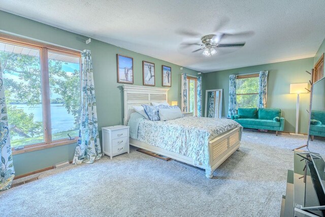 bedroom with a ceiling fan, light colored carpet, a water view, and a textured ceiling