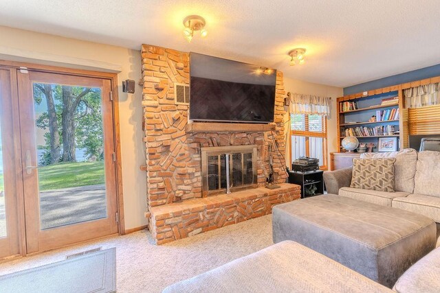 living area with a wealth of natural light, a stone fireplace, carpet, and a textured ceiling