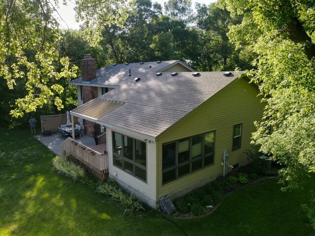 back of property with a patio, a shingled roof, a lawn, and a chimney