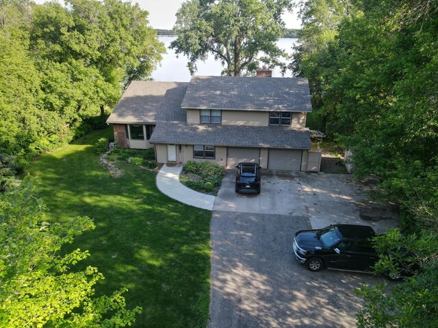 view of front facade with a front yard, concrete driveway, a chimney, and an attached garage