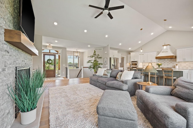 living room with light wood-type flooring, high vaulted ceiling, ceiling fan, and a fireplace