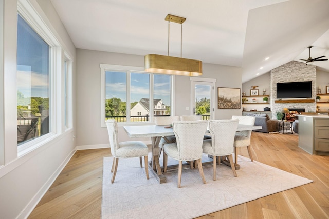 dining space featuring light hardwood / wood-style flooring, ceiling fan, a fireplace, and lofted ceiling