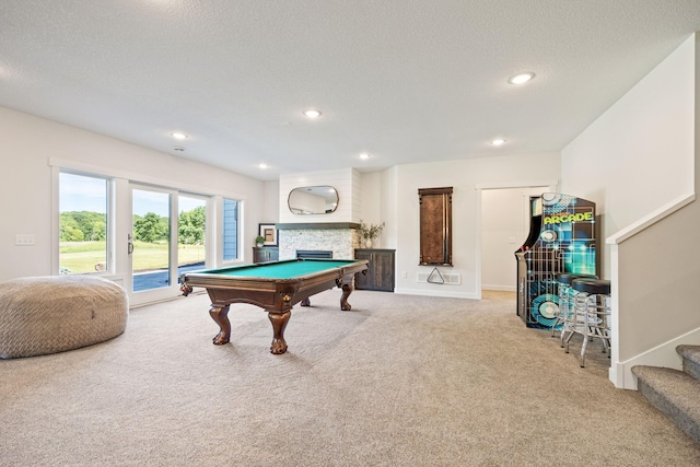 playroom featuring a textured ceiling, pool table, carpet flooring, and a stone fireplace