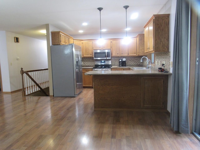 kitchen with kitchen peninsula, stainless steel appliances, sink, hardwood / wood-style floors, and hanging light fixtures