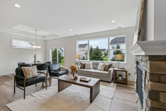 living room featuring a raised ceiling, a stone fireplace, and light hardwood / wood-style floors