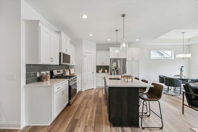 kitchen featuring light hardwood / wood-style floors, an island with sink, stainless steel appliances, sink, and decorative backsplash