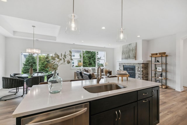 kitchen featuring a raised ceiling, light hardwood / wood-style flooring, dishwasher, a stone fireplace, and sink