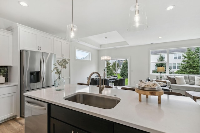 kitchen featuring light hardwood / wood-style flooring, decorative light fixtures, dishwasher, sink, and a raised ceiling