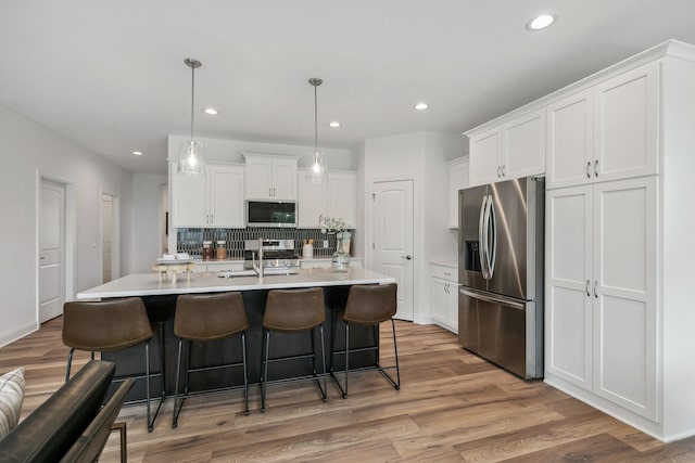 kitchen with light hardwood / wood-style flooring, appliances with stainless steel finishes, hanging light fixtures, decorative backsplash, and white cabinetry