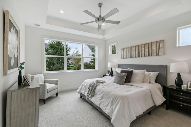 bedroom with a tray ceiling, multiple windows, and light carpet