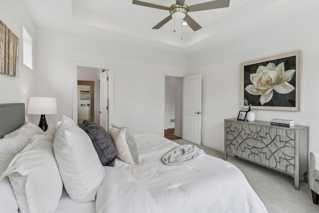 bedroom featuring a raised ceiling, ceiling fan, and light carpet