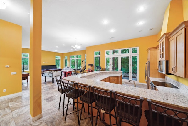 kitchen with light tile patterned floors, a breakfast bar area, an inviting chandelier, and light stone countertops