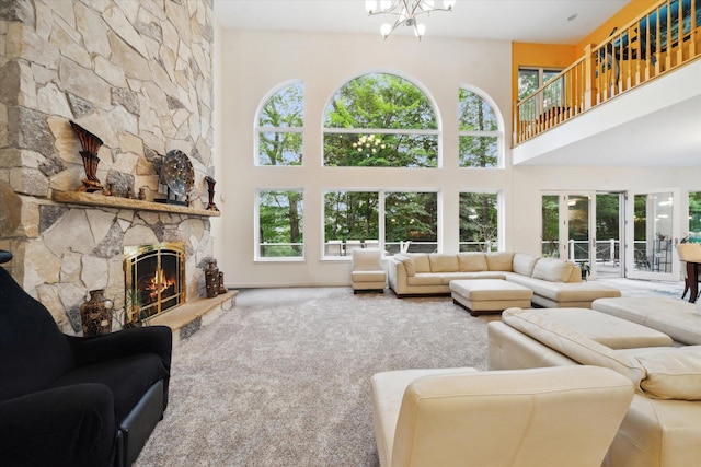 living room featuring a towering ceiling, a notable chandelier, a stone fireplace, and carpet floors