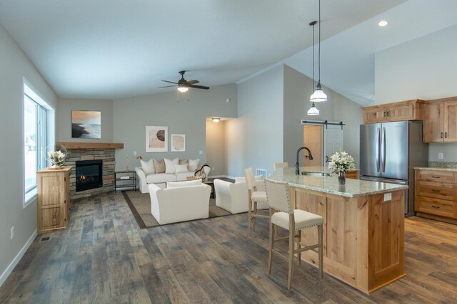 kitchen featuring decorative light fixtures, ceiling fan, a stone fireplace, stainless steel fridge, and dark wood-type flooring